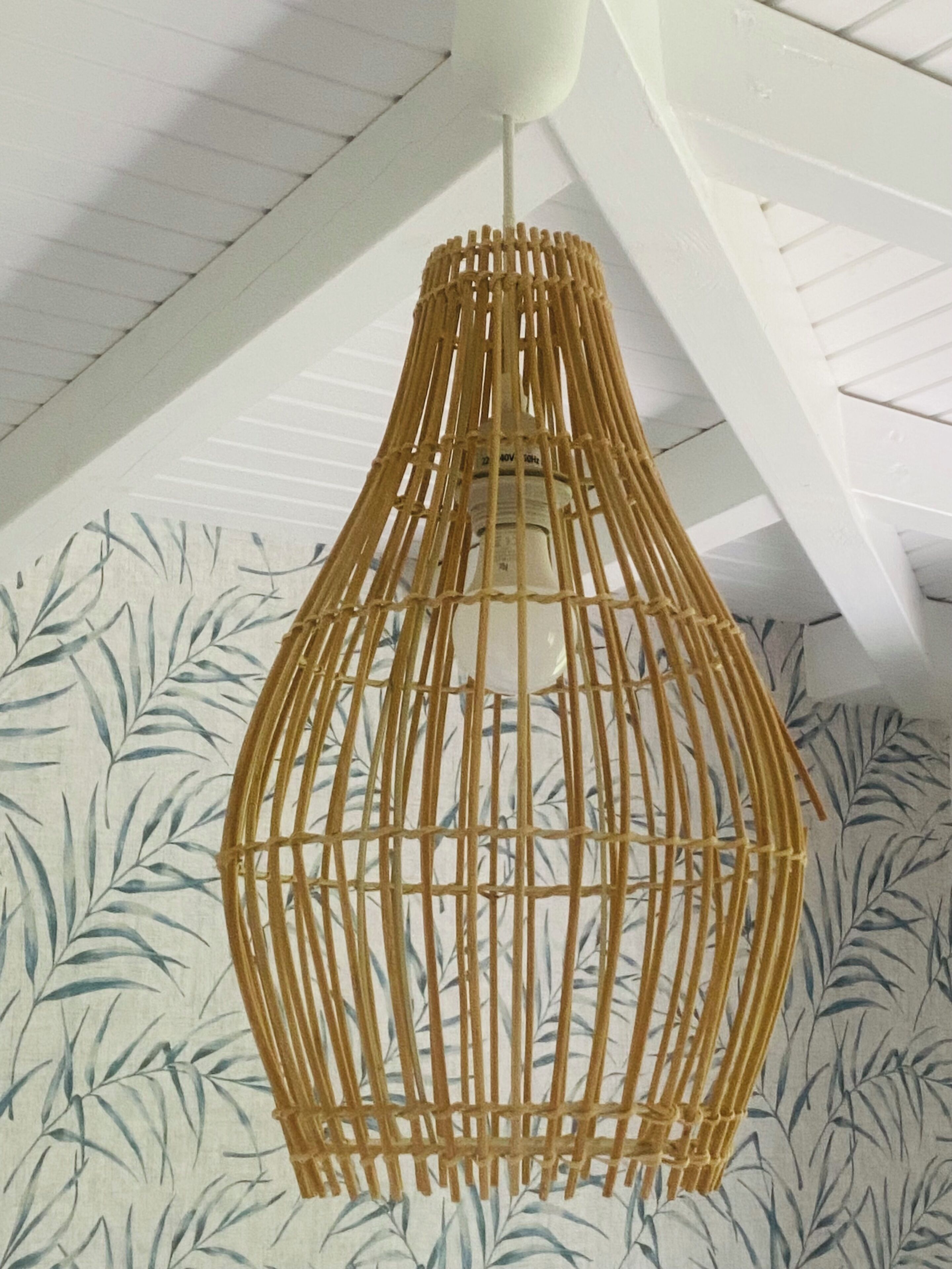 A hanging rattan light fixture with a white ceiling and bamboo leaf wallpaper.
