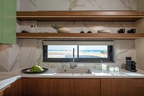 Eine moderne Küche mit großem Fenster, einer Spüle und einer Arbeitsplatte, auf der sich eine Schale mit Obst und ein Teller mit Bananen befinden.