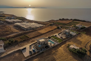 An aerial view of a coastal property with multiple buildings, a swimming pool, and a view of the sea. - Thenad Villas - Villa Theo Heated Pool, by Estia (Prinos)