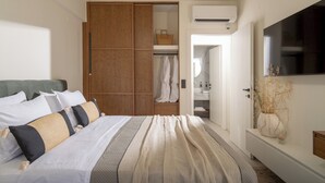 Un dormitorio con cama, armario, televisor y baño visible a través de una puerta abierta.