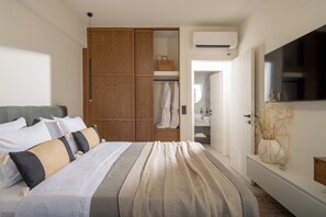 Ein Schlafzimmer mit Bett, Schrank, Fernseher und einem durchgegangenen Tür sichtbar liegenden Badezimmer.