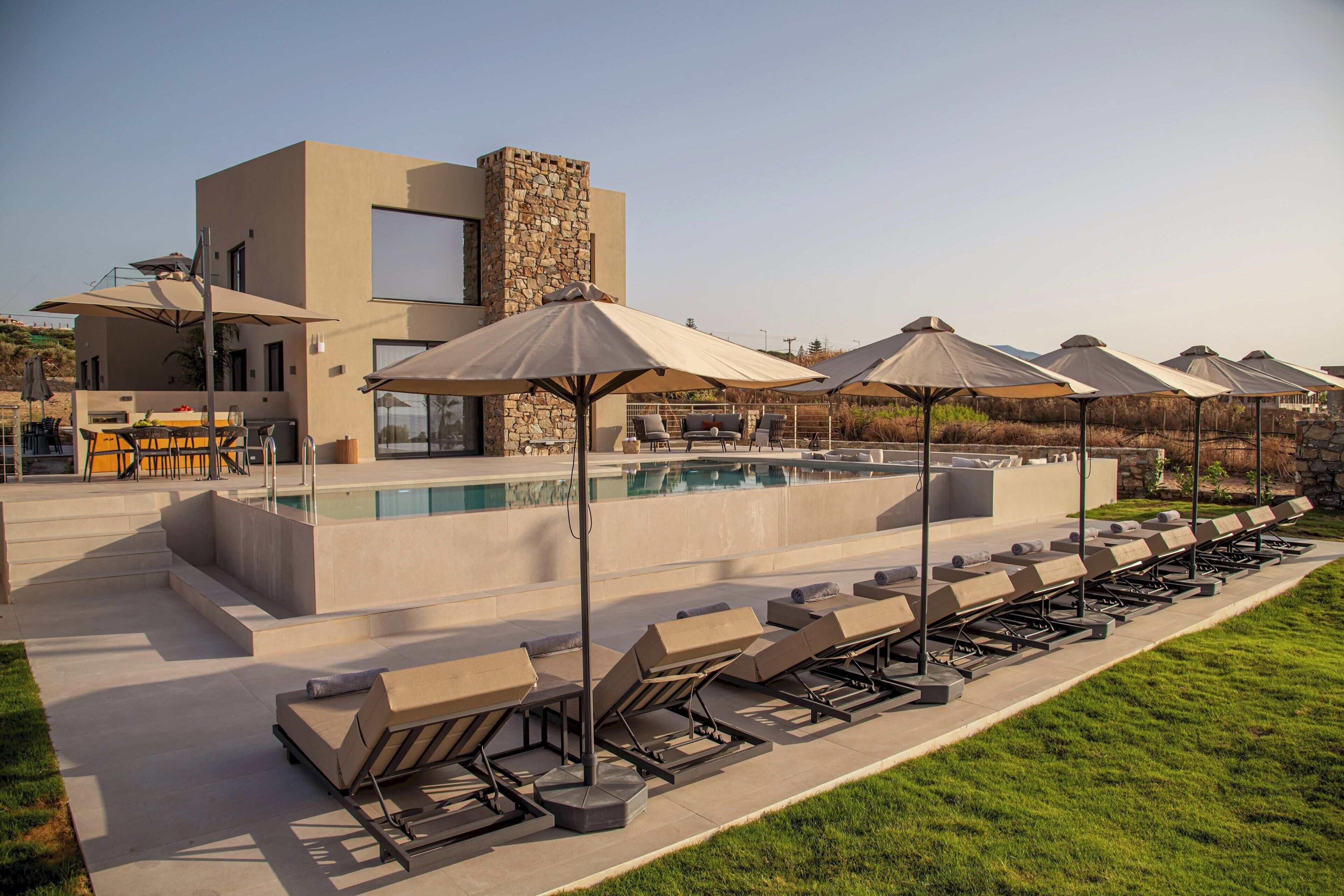 A modern outdoor pool area with lounge chairs and umbrellas, a stone wall, and a bar area.