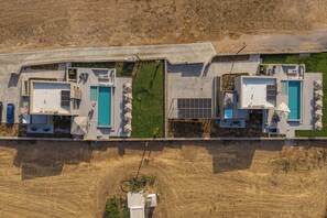 Ein modernes Gebäude mit zwei Schwimmbecken, einer überdachten Terrasse und Blick auf eine trockene, grasbewachsene Landschaft.