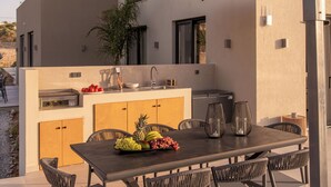 Un área de cocina al aire libre con una mesa de comedor, sillas y una variedad de frutas.