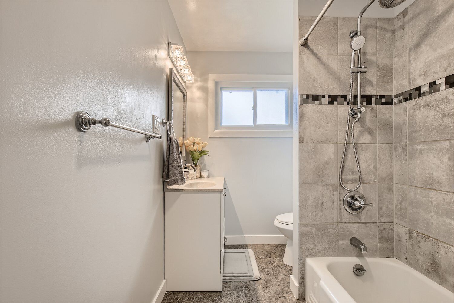 A bathroom with a shower, toilet, and sink, with a window providing natural light.