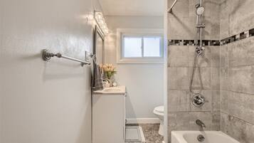 A bathroom with a shower, toilet, and sink, with a window providing natural light.