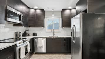 A modern kitchen with dark cabinetry, stainless steel appliances, and a window with blinds.