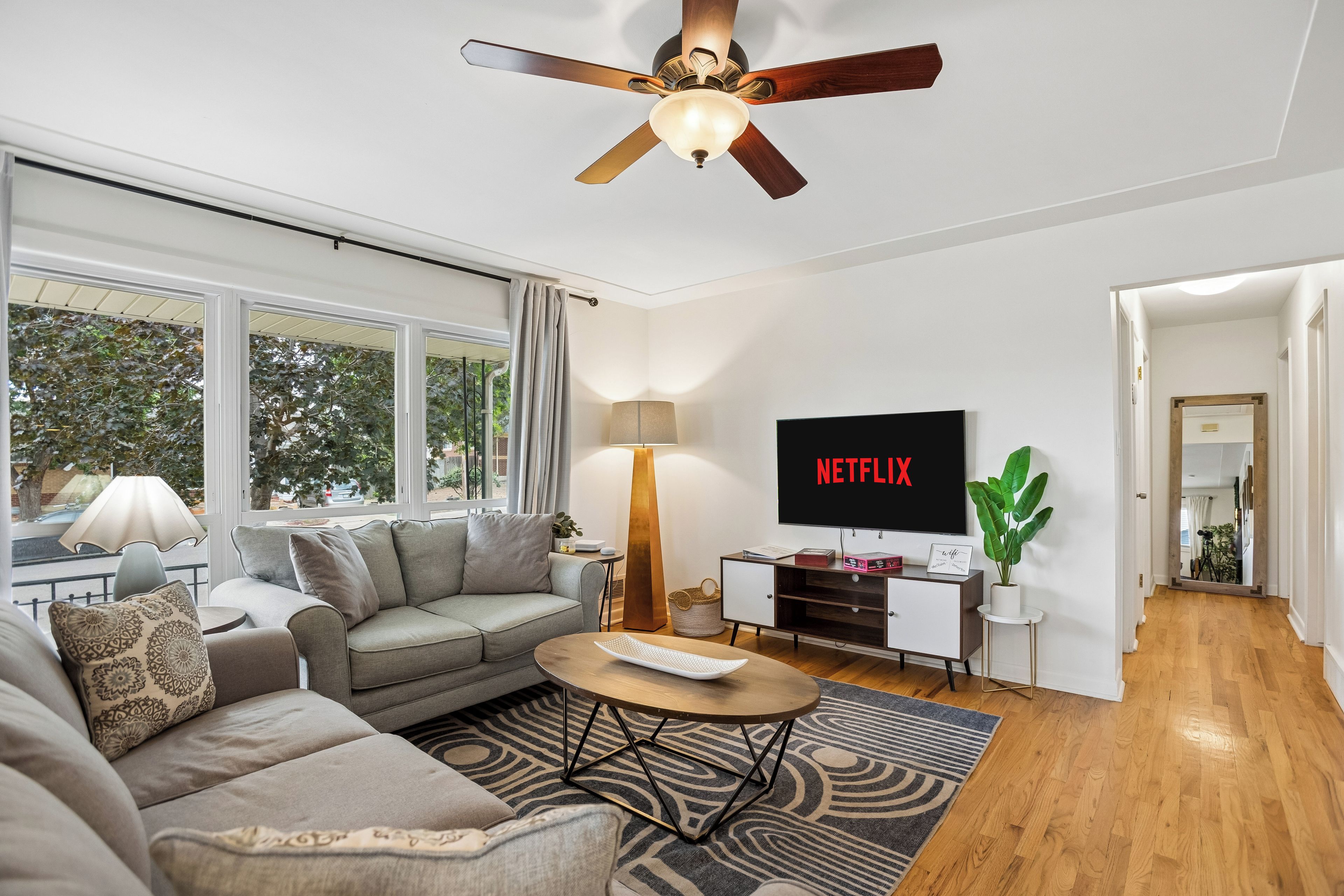 A modern living room with a grey sofa, a coffee table, a TV, and a ceiling fan.