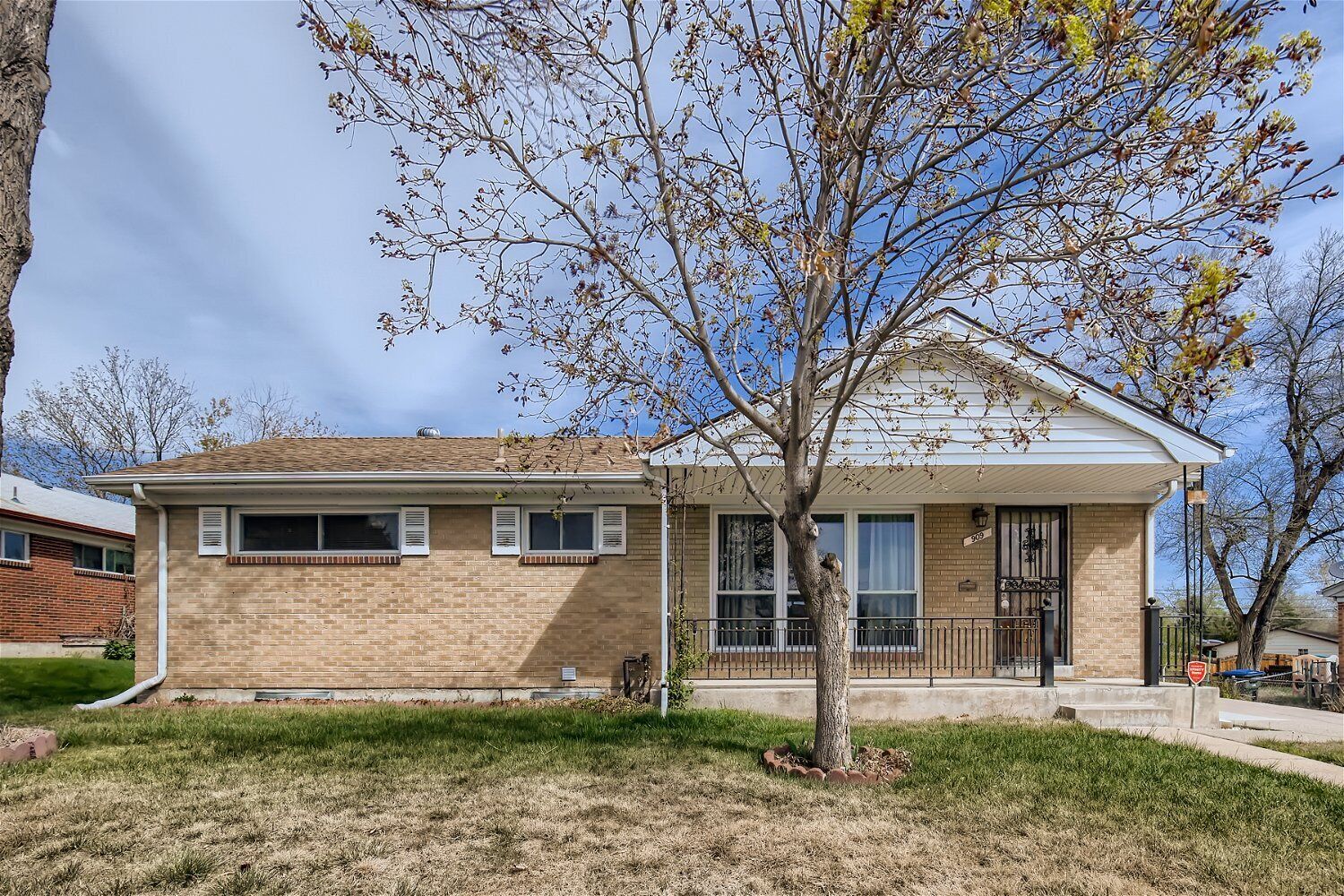A two-story house with a brick facade, a front porch, and a tree in front.