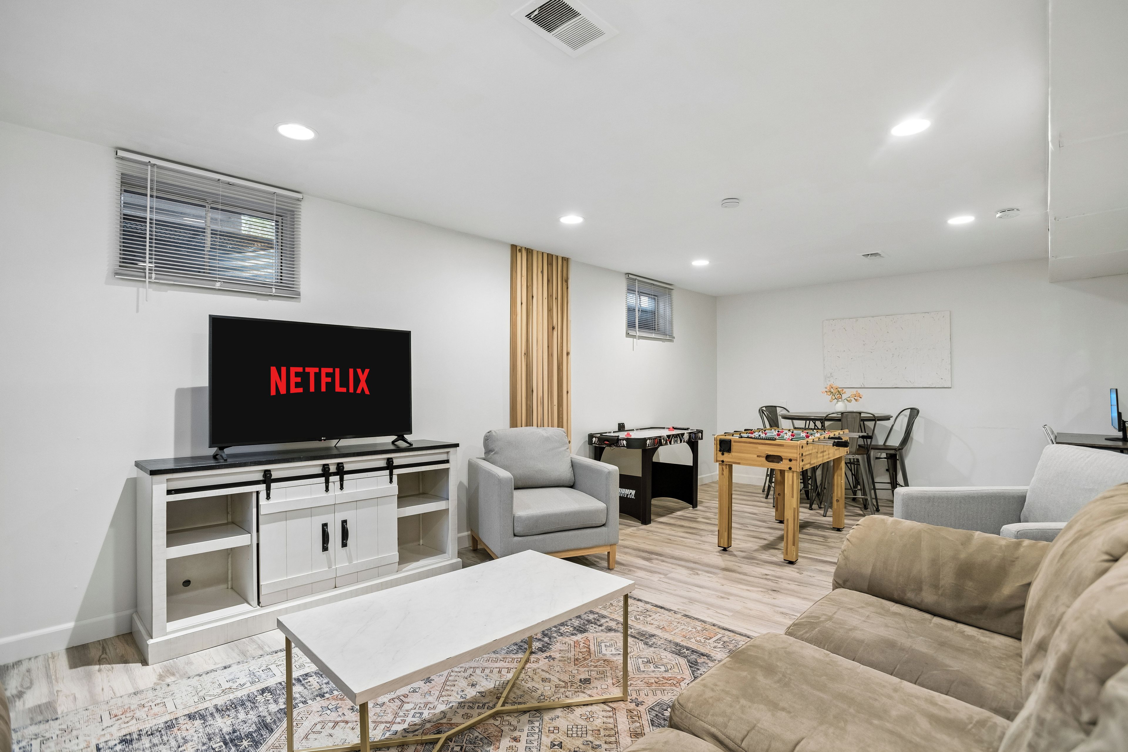 A modern living room with a flat-screen TV, a sofa, a coffee table, and a foosball table.