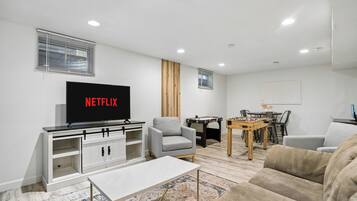 A modern living room with a flat-screen TV, a sofa, a coffee table, and a foosball table.