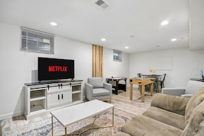 A modern living room with a flat-screen TV, a sofa, a coffee table, and a foosball table. - Denver Retreat with Hot Tub, Sauna, Game Room, & 5BR (Northglenn)