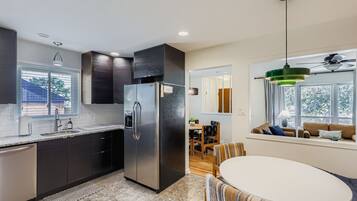 A modern kitchen with dark cabinetry, a stainless steel refrigerator, and a dining area with a round table and striped chairs.