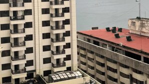Um edifício alto com várias varandas, uma estrutura com telhado vermelho em primeiro plano e um corpo d'água ao fundo.