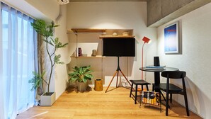 A modern room with a flat-screen TV, a tripod stand, a small table with chairs, and a potted plant. - Tora Hotel Shiba (Minato City)