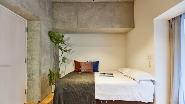A bedroom with a bed, a plant, and a concrete wall. - Tora Hotel Shiba (Minato City)