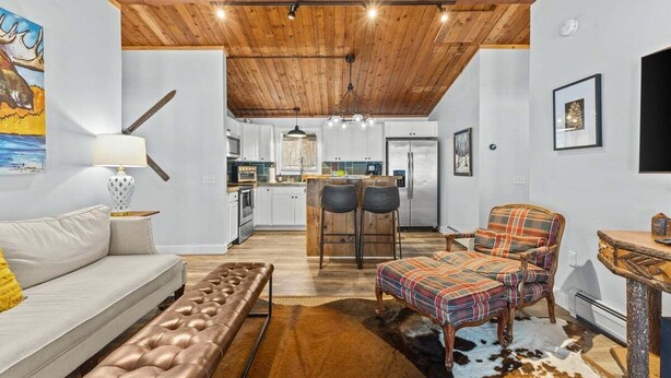 Ein modernes Interieur mit Holzboden, einer Couch, einer Bank, einem Essbereich mit Stühlen und einer Küche im Hintergrund.