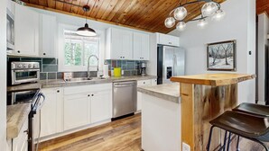 Eine moderne Küche mit weißen Schränken, Edelstahlgeräten, einer Holzbalkendecke und einer Bar.