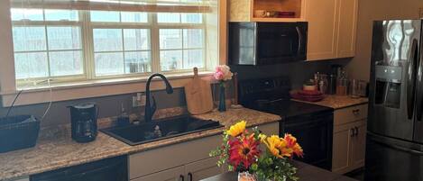 A kitchen with a window, a sink, a microwave, a refrigerator, and a dining table with flowers.