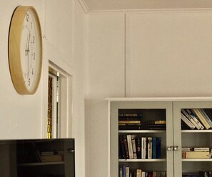 Ein Zimmer mit einer hölzernen Wanduhr, einem Bücherregal mit verschiedenen Büchern und einem weißen Schrank.
