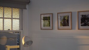 A room with a window, a lamp, and three framed pictures on the wall. - Mallee Drift - Exhale and Relax (James Well)