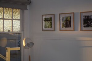 A room with a window, a lamp, and three framed pictures on the wall. - Mallee Drift - Exhale and Relax (James Well)