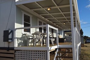 A covered porch with outdoor seating, a wooden deck, and a white exterior.