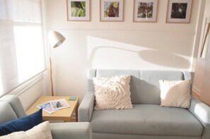 A living room with a sofa, a table with a lamp, and framed pictures on the wall.