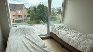 Un dormitorio con dos camas, un ventanal y vistas a un edificio de ladrillo y árboles.