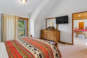 A bedroom with a large bed, a wooden dresser, a television, and a view of a pool table through a mirror. - Mountaintop retreat with 5 bedrooms, hot tub, pool table, and community pool! (McHenry)