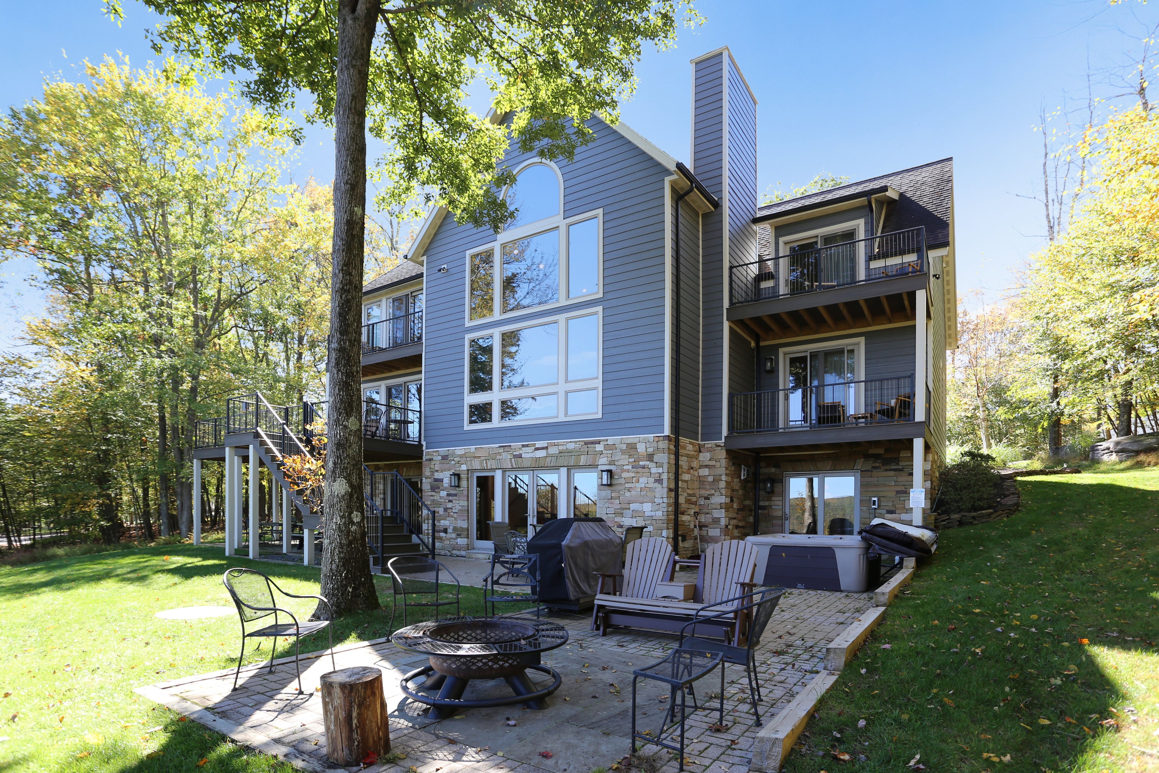 A two-story house with a stone facade, a patio with outdoor furniture, and a fire pit.