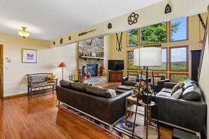 Un salon spacieux doté d’une cheminée en pierre, de canapés en cuir et de grandes fenêtres offrant une vue sur l’extérieur.