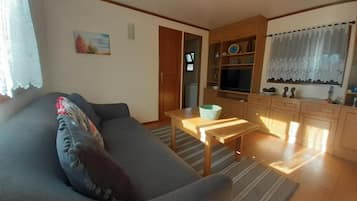 A living room with a sofa, a small table, and a kitchen area with cabinets and a window.