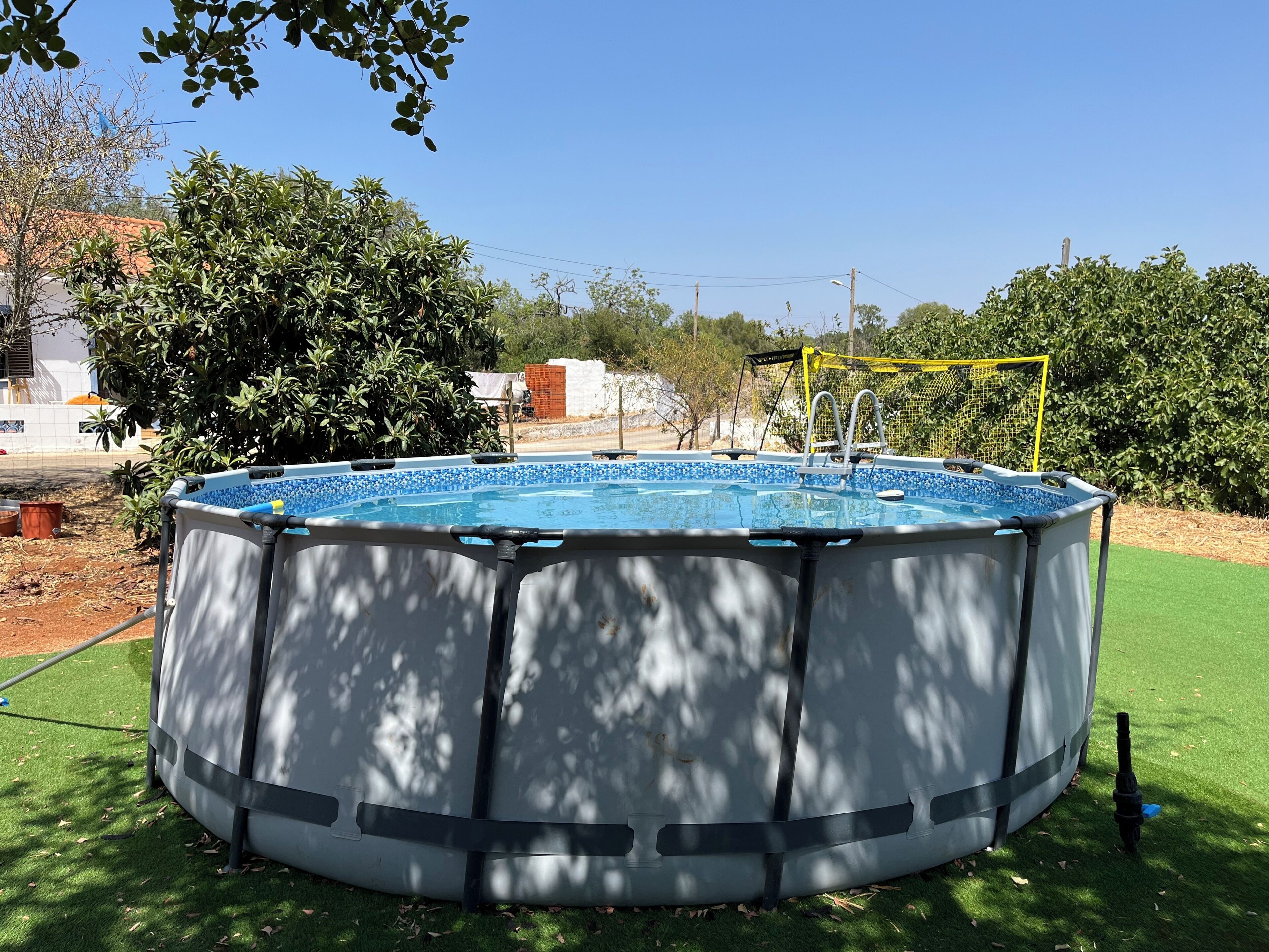 Une piscine hors sol, protégée par un filet de sécurité, entourée de pelouse verdoyante et d’arbres.