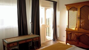Ein Zimmer mit einem Bett, einem Schreibtisch, einem Kleiderschrank und einer Tür zu einem Außenbereich.