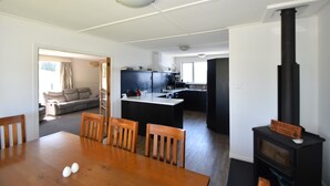 A modern kitchen with a central island, a dining area with a wooden table and chairs, and a black wood stove.