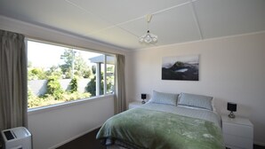 A bedroom with a bed, a window, a nightstand, a lamp, and a painting on the wall.