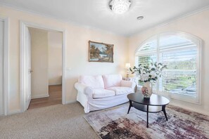 A room with a white sofa, a round table with a vase, a painting on the wall, and a large window. - Panoramic Bayview spacious Home & Garden (Mount Martha)