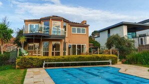Una casa moderna de dos pisos con piscina, ventanas amplias y un jardín cuidado.