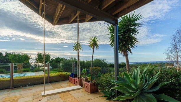 Un espacio al aire libre techado con una hamaca, plantas en macetas y vistas al paisaje.