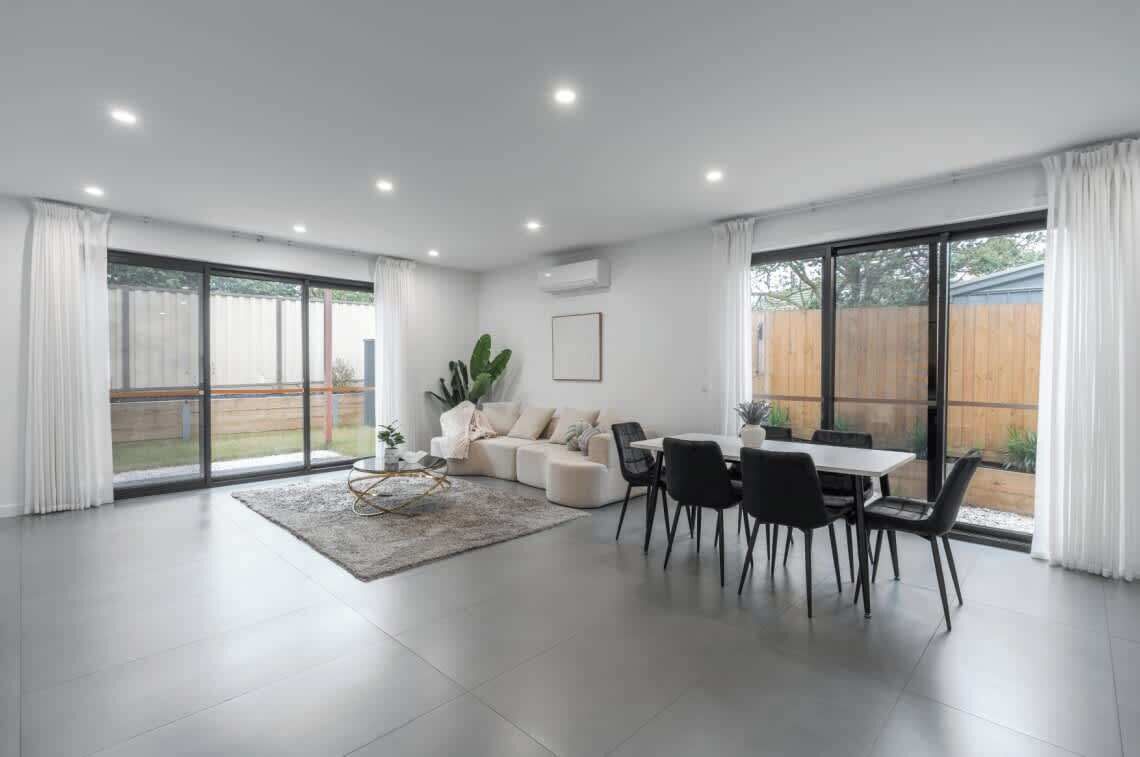A spacious living room with a dining area, large windows, and a sliding glass door leading to a backyard.