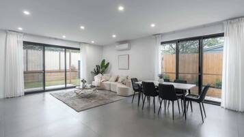 A spacious living room with a dining area, large windows, and a sliding glass door leading to a backyard.