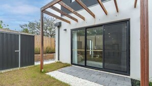 Una casa moderna con un amplio ventanal corredero, una pérgola de madera y un patio empedrado.
