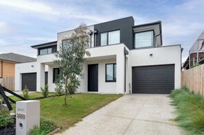 Ein modernes, zweistöckiges Haus mit Auffahrt, Garage und einem kleinen Baum im Vorgarten.