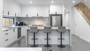 Una cocina moderna con armarios blancos, un refrigerador de acero inoxidable y tres taburetes de bar.