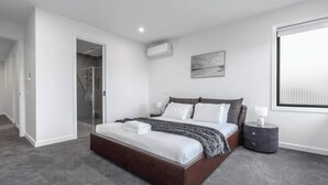 Un dormitorio moderno con una cama grande, una mesita de noche, un equipo de aire acondicionado y una ventana con vistas.