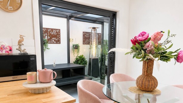 Eine moderne Küche mit einem Glastisch und rosa Stühlen, einer Mikrowelle und einer Vase mit Blumen.