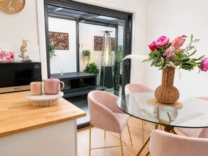 A modern kitchen with a glass table and pink chairs, a microwave, and a vase with flowers. - Holiday House in Laverton Modern Comfort ,walk to Train Station,car Hire Option (Melbourne)