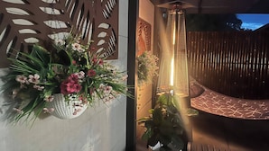 Ein Zimmer mit einer dekorativen Wandverkleidung, einer hängenden Blumenkomposition, einer vertikalen Leuchte und einer gepolsterten Sitzgruppe.