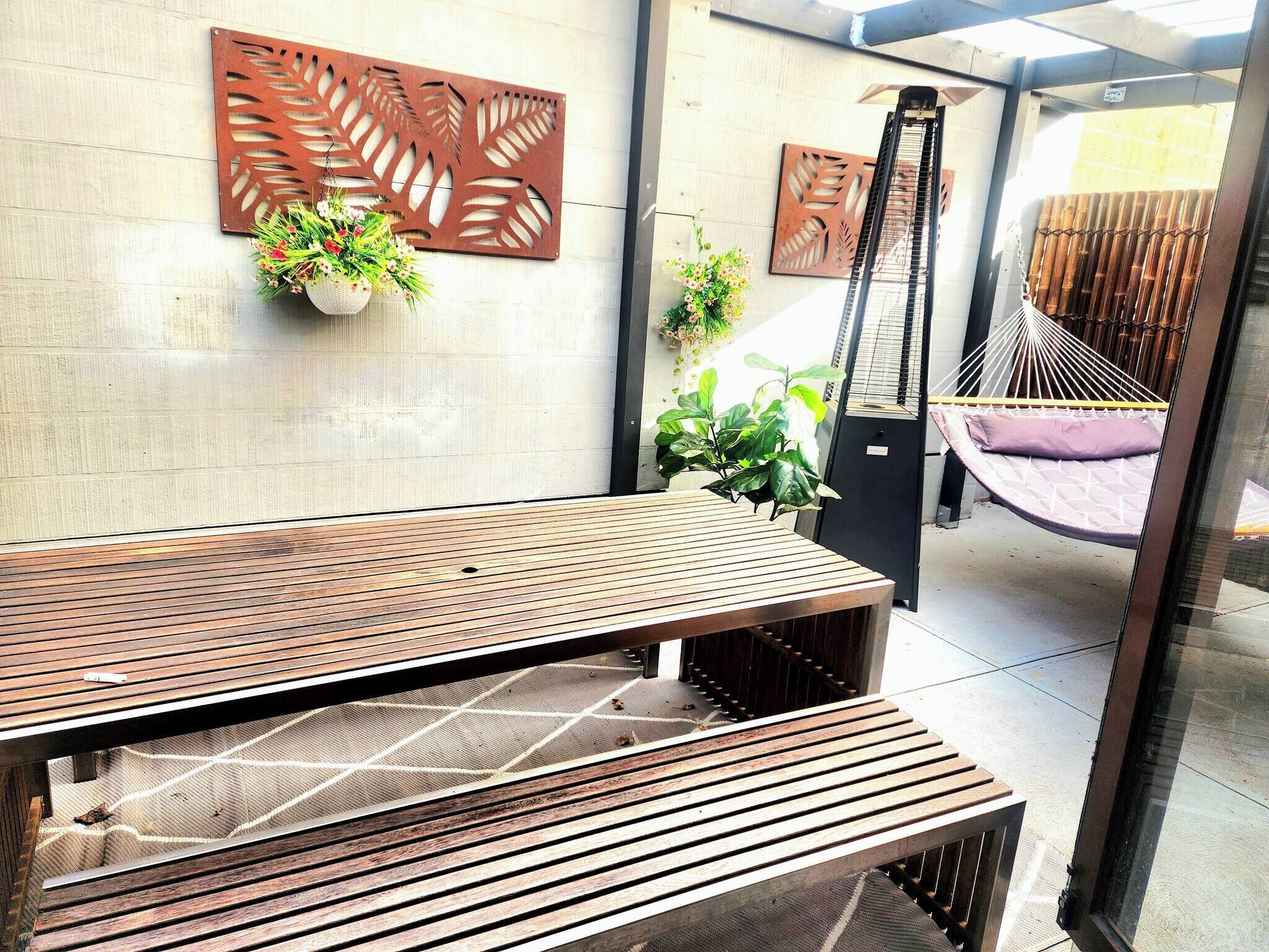 A wooden bench, a hanging plant, and a hammock in a sunlit outdoor area.